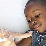 Close-up of a little black boy smiling as he receives a vaccine.