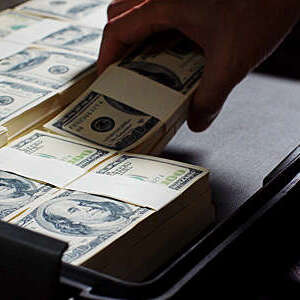 Close-up of hand putting bundles of hundred dollar bills in a briefcase.