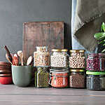 Jars of pulses and cereals stacked on a table alongside wooden bowls and kitchen utensils.