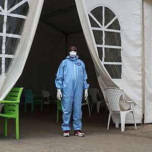 Doctor in blue overalls, gloves and mask stands at the entrance of a tent health centre in Djibouti