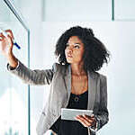 Shot of a young businesswoman using a digital tablet while writing notes on a glass wall in an office.