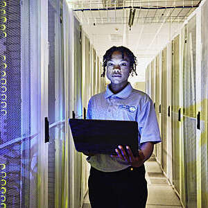 Medium shot portrait of female IT professional holding laptop while standing in row of servers in data center