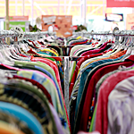 a variety of colorful shirts hang on a clothing rack at a thrift store