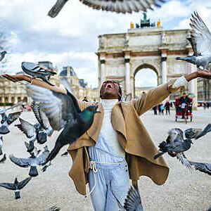 France, Paris, Young smiling woman among doves flying in front of Triumph arch of Carousel.