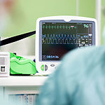 Cardiogram monitor in surgery while not recognizable doctor operates. The focus is on the screen